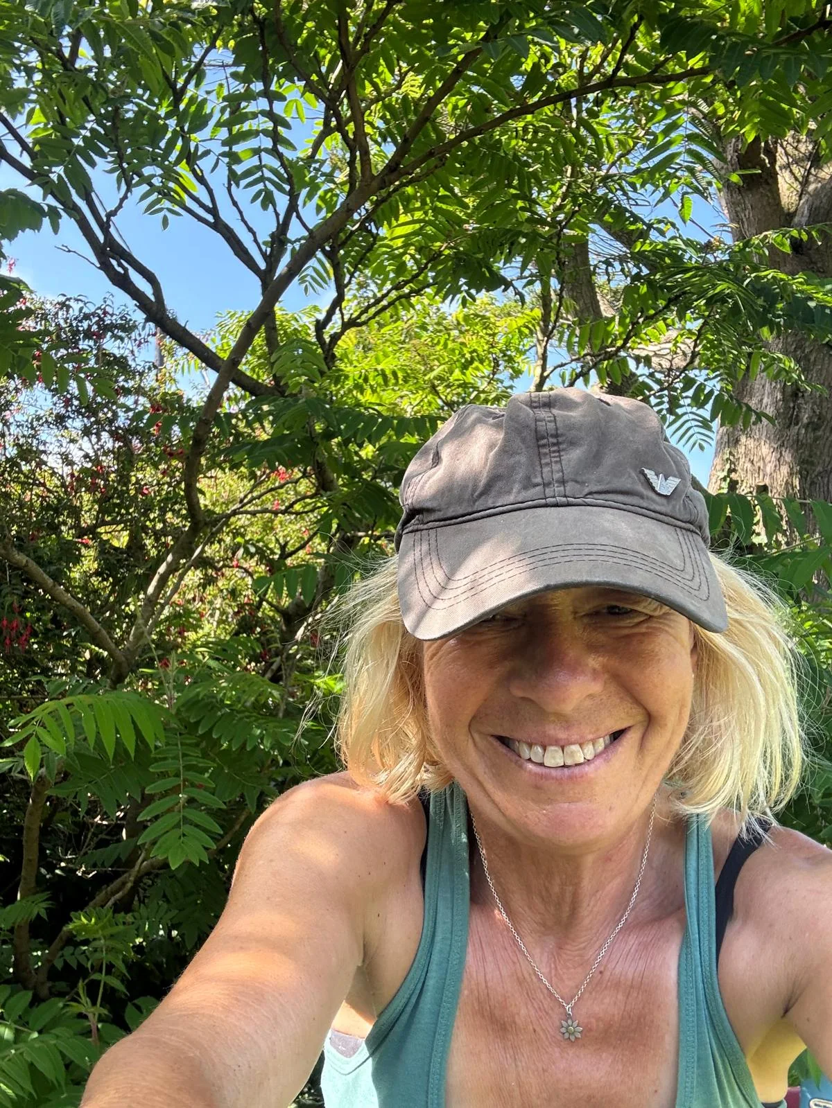 The Curious Garden designer smiling beneath a canopy of green leaves