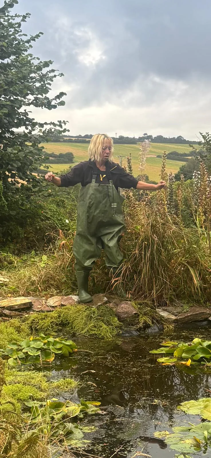 The Curious Garden designer standing in green waders beside a pond