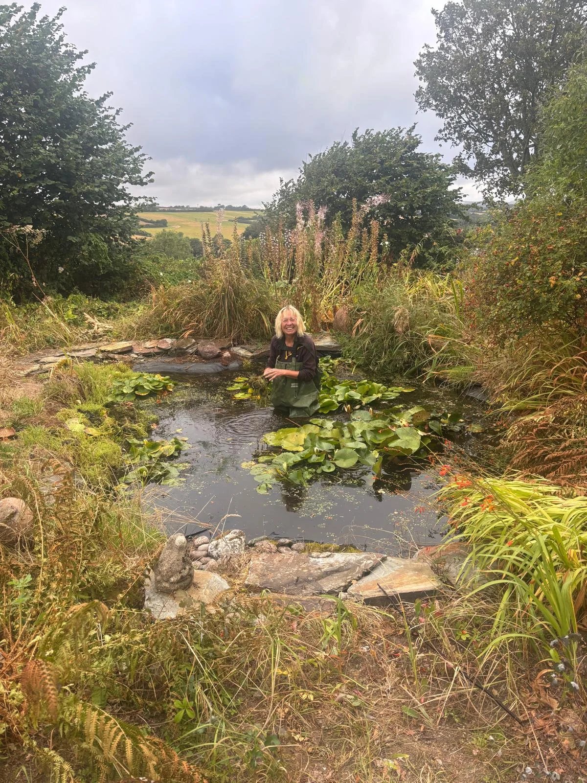 The Curious Garden designer smiling while working among pond plants